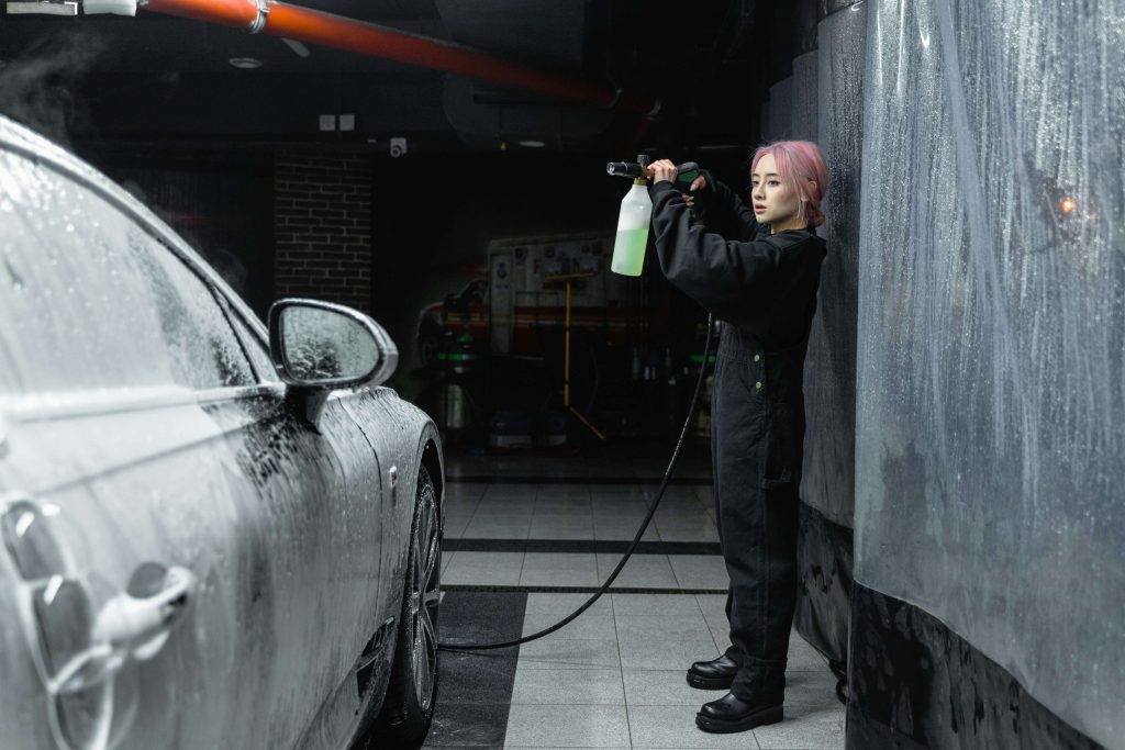 Woman using pressure washer to clean a car with soap