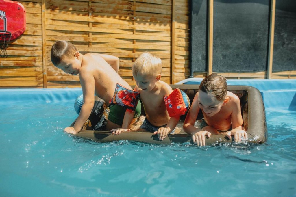 3 boys playing in an above ground pool with a floatie.